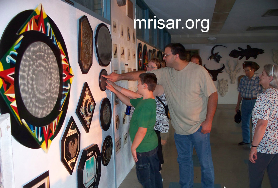 Visitors to MRISAR are seen  here touching the etched Braille poem that accompanies “Siren in Metal” an original etched aluminum wall hanging sculpture by Victoria Lee Croasdell, an awarded, published and exhibited; multi-disciplined artist, photographer, writer, poet and engineer.  This piece is made of a hand etched aluminum mounted on M.D.O. that is painted with acrylic. Size 18" wide x 15" high, created in 1996. It is based on European mythology. Its etched aluminum oval poem in braille accompanies it to complete its total form as Illustrated Poetry. Victoria, a multi-awarded poet, writes poetry for all her art pieces and many of her photography pieces, thus adding an extra dimension or understanding into her conception of its particular creation.